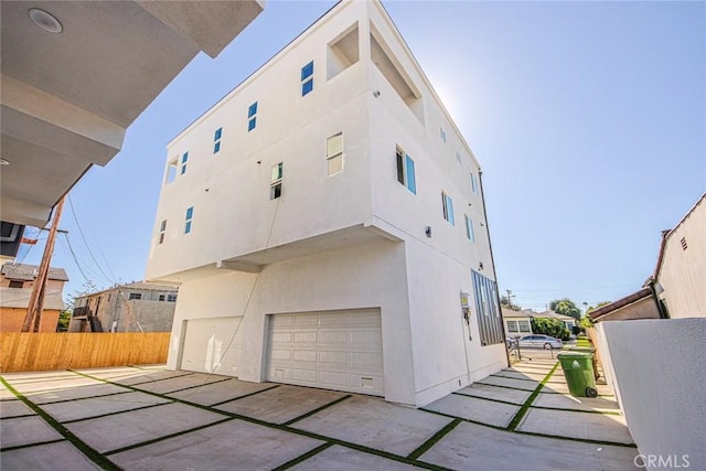 back of house featuring a garage, fence, and stucco siding