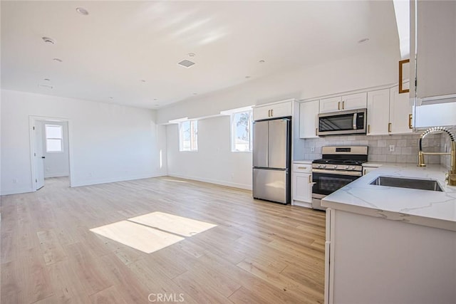 kitchen featuring light stone counters, a sink, light wood-style floors, appliances with stainless steel finishes, and decorative backsplash