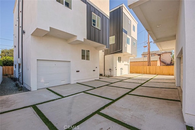 exterior space featuring a garage, board and batten siding, fence, and stucco siding