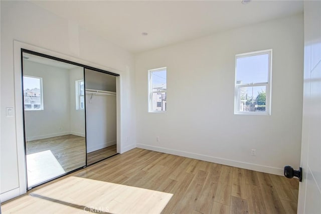 unfurnished bedroom with light wood finished floors, multiple windows, baseboards, and a closet