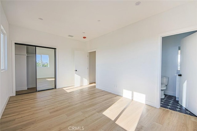 unfurnished bedroom featuring light wood-style flooring, connected bathroom, visible vents, and a closet