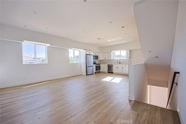 interior space featuring light wood finished floors, tasteful backsplash, stainless steel appliances, light countertops, and white cabinetry