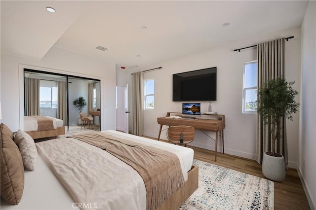 bedroom featuring multiple windows, visible vents, baseboards, and wood finished floors