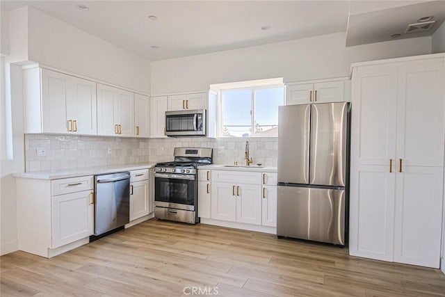 kitchen with light wood finished floors, stainless steel appliances, light countertops, white cabinetry, and a sink