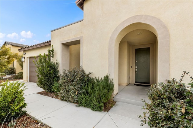 doorway to property with a garage, a tile roof, and stucco siding