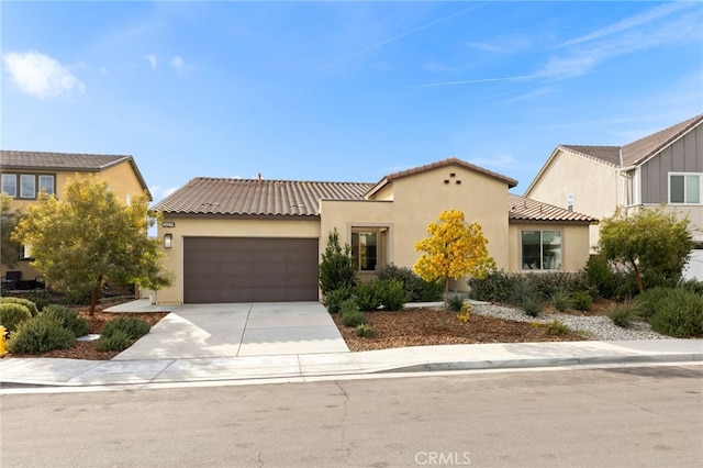 mediterranean / spanish-style home with an attached garage, a tiled roof, concrete driveway, and stucco siding