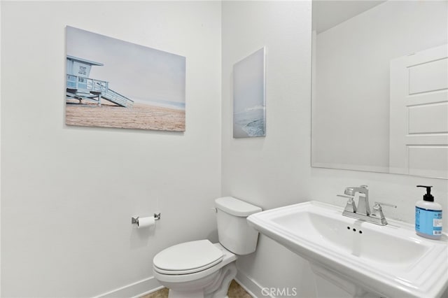 half bathroom with a sink, toilet, and baseboards