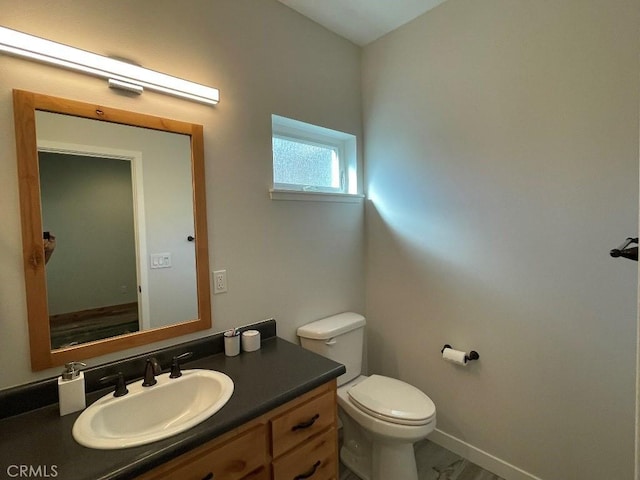 half bath with baseboards, vanity, and toilet