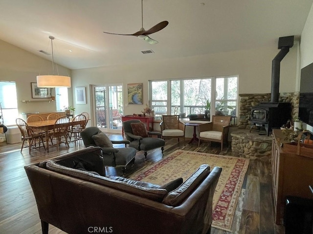 living room featuring a wood stove, visible vents, vaulted ceiling, and wood finished floors