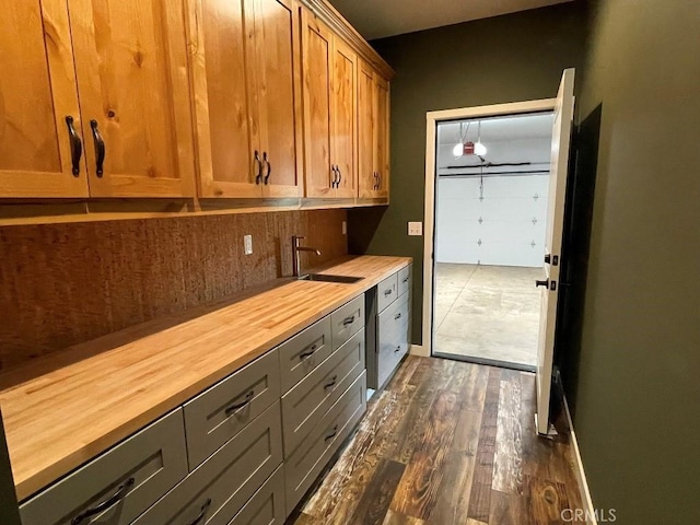 interior space featuring butcher block countertops, dark wood-type flooring, a sink, baseboards, and tasteful backsplash