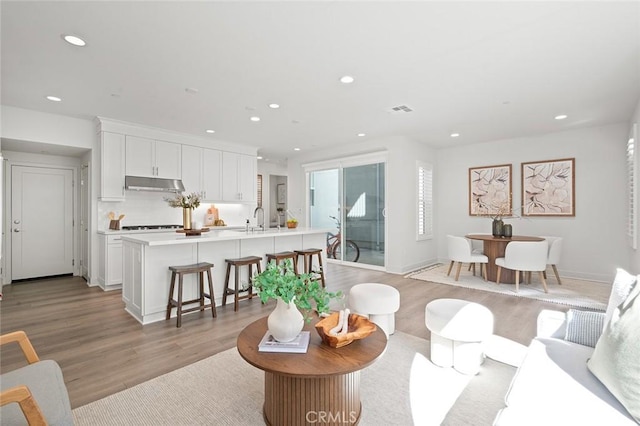 living area with light wood-type flooring, visible vents, baseboards, and recessed lighting