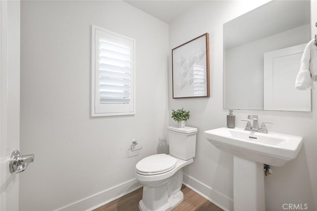 half bath with a sink, wood finished floors, toilet, and baseboards