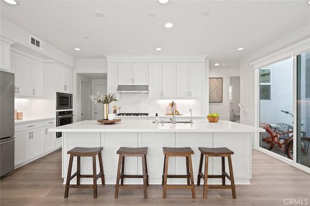 kitchen with under cabinet range hood, a sink, visible vents, a kitchen breakfast bar, and appliances with stainless steel finishes