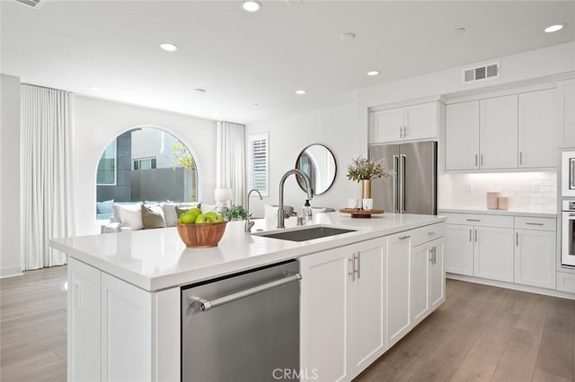 kitchen with light wood-style flooring, a sink, visible vents, appliances with stainless steel finishes, and an island with sink