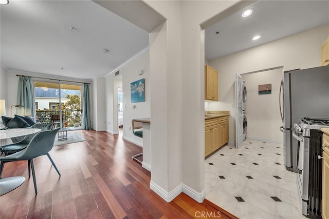 kitchen with light brown cabinets, baseboards, open floor plan, stainless steel gas stove, and crown molding