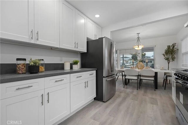 kitchen with pendant lighting, light wood finished floors, dark countertops, appliances with stainless steel finishes, and white cabinets