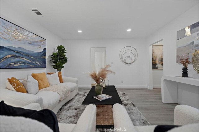 living room featuring baseboards, visible vents, wood finished floors, and recessed lighting