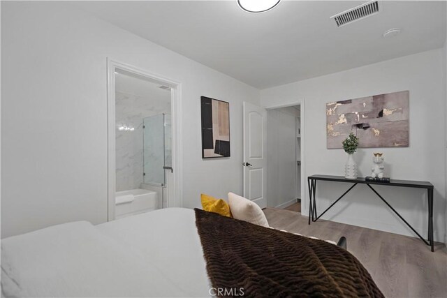 bedroom with visible vents, ensuite bath, and wood finished floors