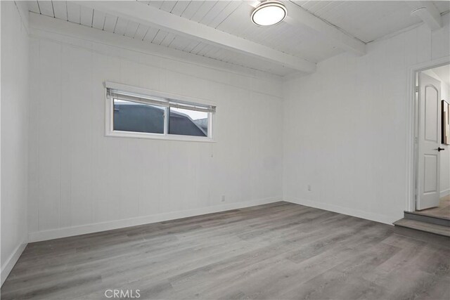 spare room with wood finished floors, beam ceiling, and baseboards