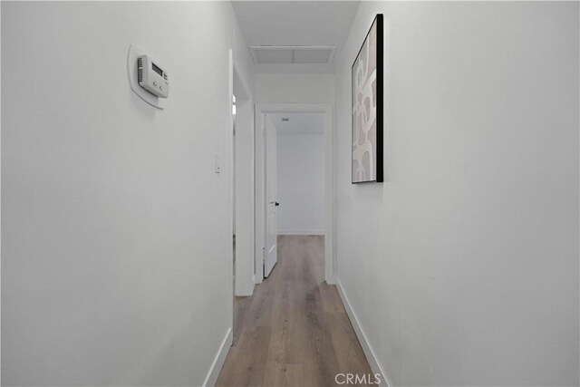 hall with attic access, light wood-type flooring, visible vents, and baseboards