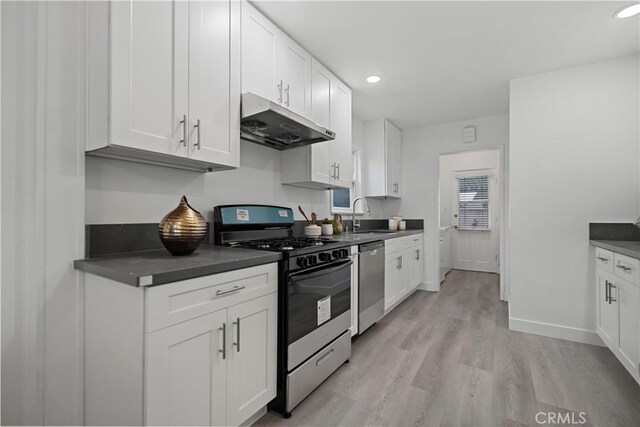 kitchen with dark countertops, under cabinet range hood, white cabinetry, and appliances with stainless steel finishes