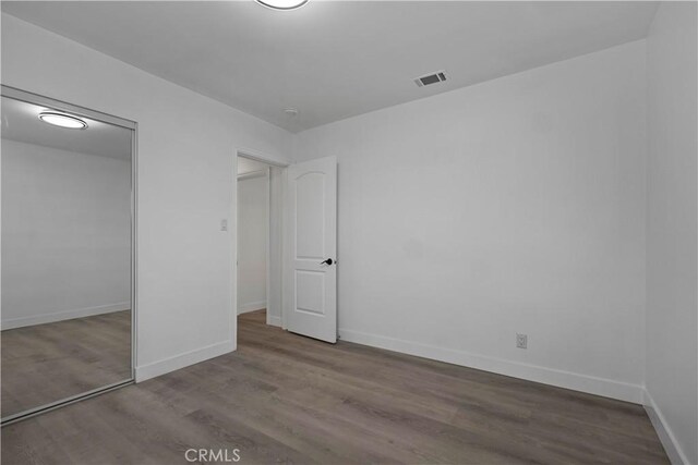 unfurnished bedroom with a closet, visible vents, baseboards, and wood finished floors