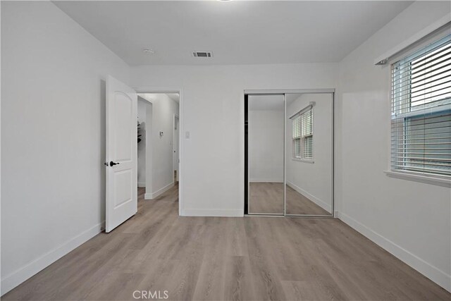 unfurnished bedroom with visible vents, a closet, baseboards, and wood finished floors