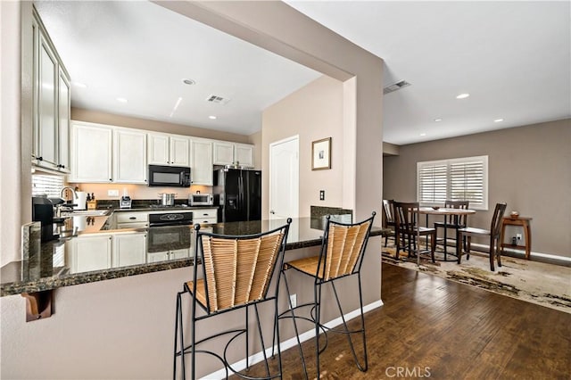 kitchen featuring visible vents, dark wood finished floors, a peninsula, and black appliances