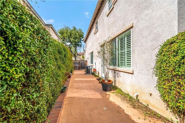 view of side of property featuring a patio area, fence, cooling unit, and stucco siding