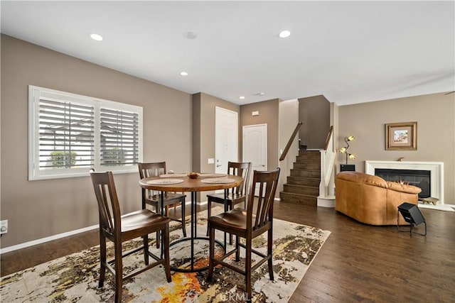 dining room featuring wood finished floors, stairway, a glass covered fireplace, and recessed lighting