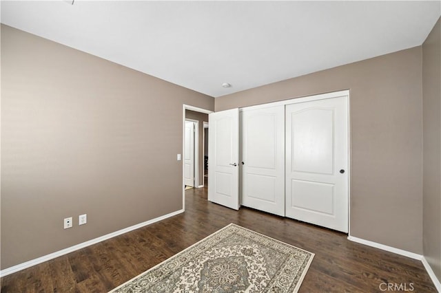 unfurnished bedroom featuring a closet, dark wood finished floors, and baseboards