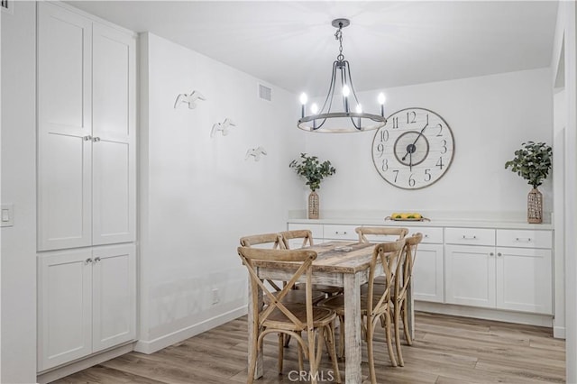 dining area featuring light wood-type flooring, visible vents, a notable chandelier, and baseboards