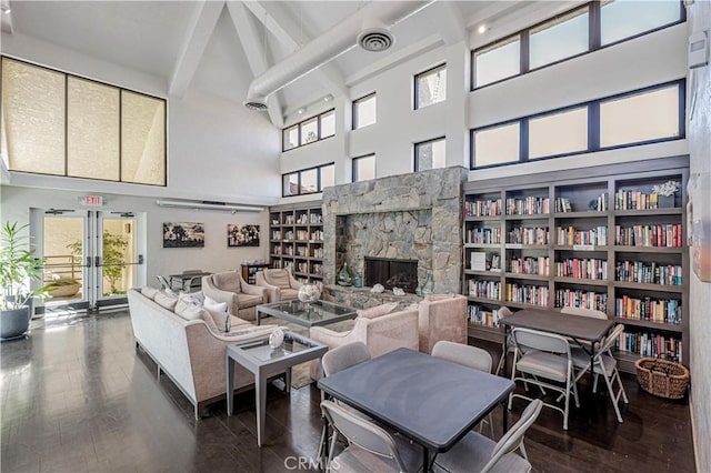 living room featuring beam ceiling, french doors, visible vents, a stone fireplace, and wood finished floors