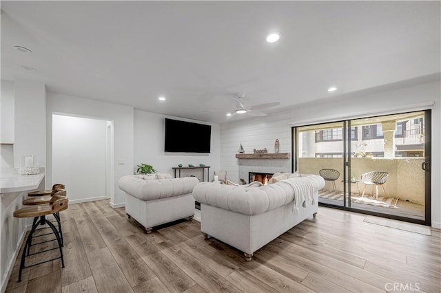 living room featuring ceiling fan, a lit fireplace, recessed lighting, and light wood-style floors