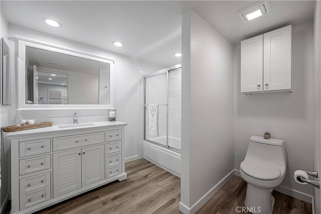 bathroom featuring baseboards, toilet, enclosed tub / shower combo, wood finished floors, and vanity