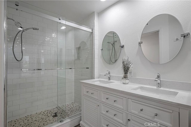 bathroom with a stall shower, a sink, and double vanity