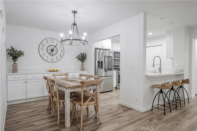 dining room with light wood-style flooring, baseboards, and an inviting chandelier