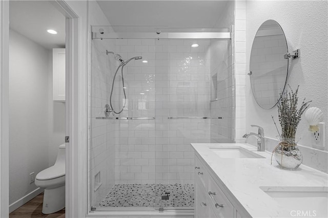 full bath with double vanity, toilet, wood finished floors, a shower stall, and a sink