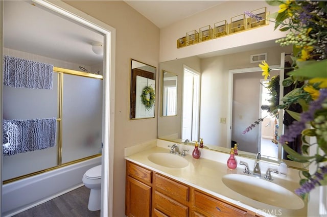 full bathroom featuring double vanity, enclosed tub / shower combo, toilet, and a sink