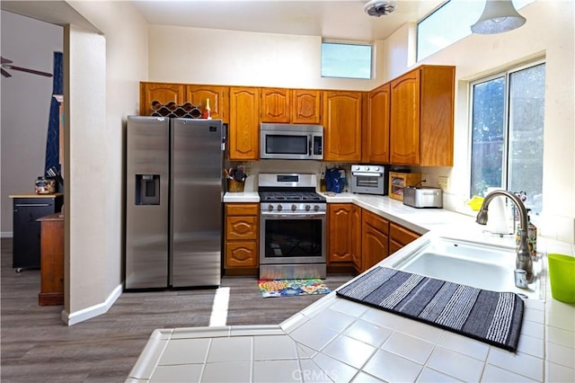 kitchen featuring baseboards, brown cabinets, appliances with stainless steel finishes, wood finished floors, and a sink