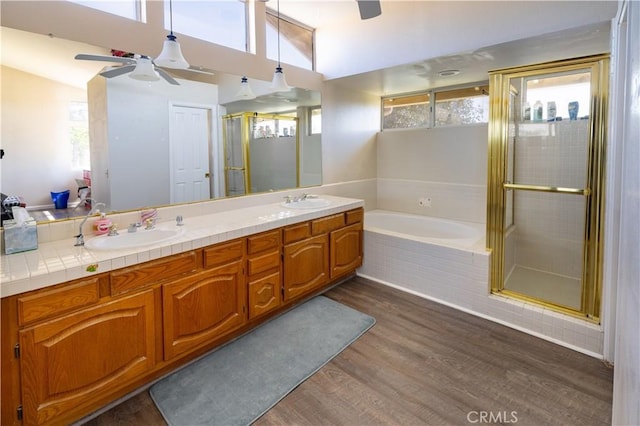 bathroom with a shower stall, double vanity, wood finished floors, a bath, and a sink