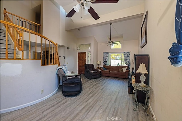 living area with a ceiling fan, wood finished floors, baseboards, high vaulted ceiling, and stairs