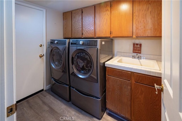 clothes washing area featuring washer and clothes dryer, light wood-style flooring, cabinet space, and a sink