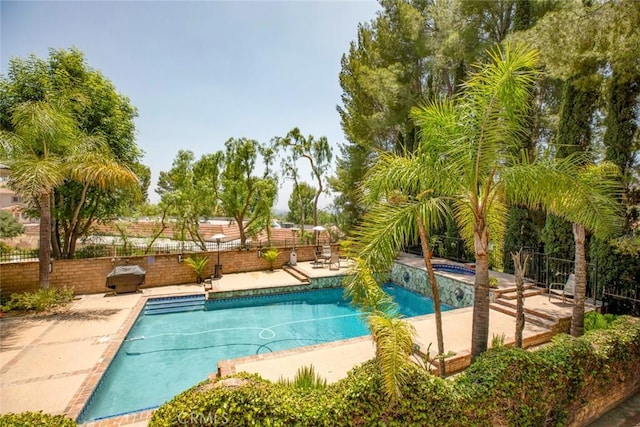 view of swimming pool featuring a pool with connected hot tub, fence, and a patio