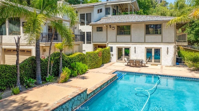 rear view of property with french doors, stucco siding, a patio area, a balcony, and a tiled roof