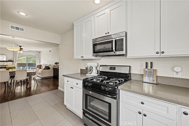 kitchen with visible vents, light tile patterned floors, white cabinets, stainless steel appliances, and a ceiling fan