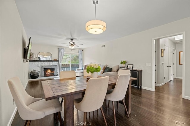 dining area with visible vents, baseboards, a fireplace, a ceiling fan, and dark wood-style flooring