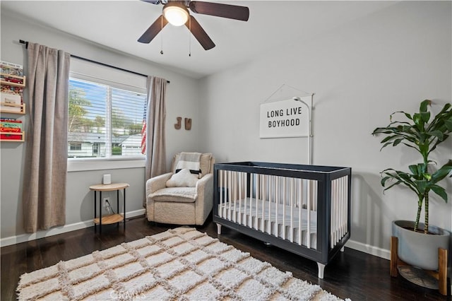 bedroom with ceiling fan, a crib, baseboards, and wood finished floors