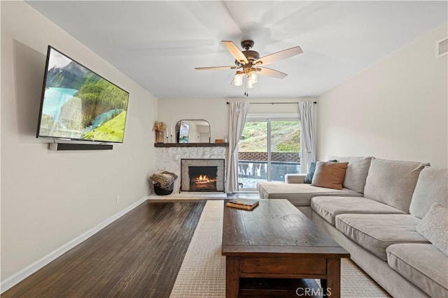 living room with a ceiling fan, visible vents, baseboards, a fireplace, and dark wood-style flooring