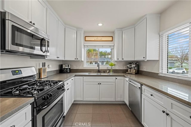 kitchen featuring a sink, appliances with stainless steel finishes, light tile patterned floors, and white cabinetry